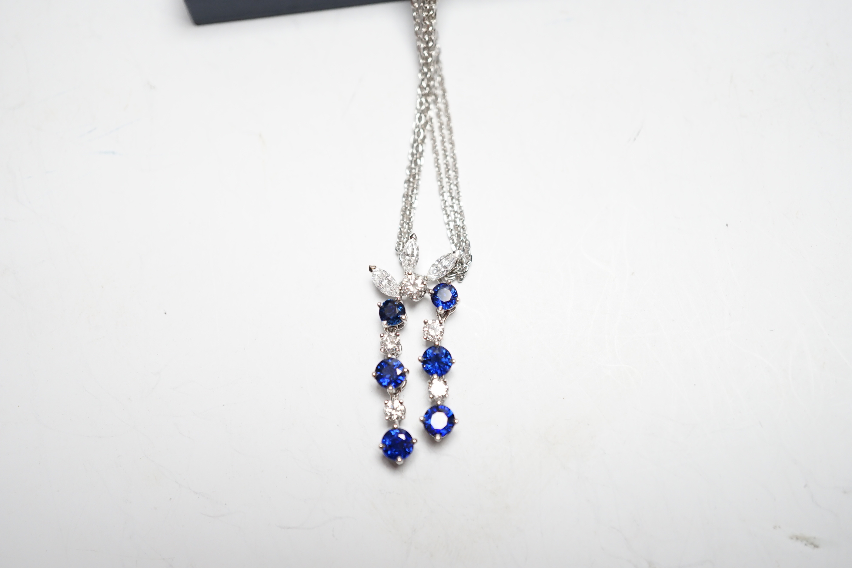 A modern 750 white metal, sapphire and diamond set cluster pendant, 31mm, on a twin strand white metal chain, 44cm, gross weight 10.3 grams, in a Bucherer box.